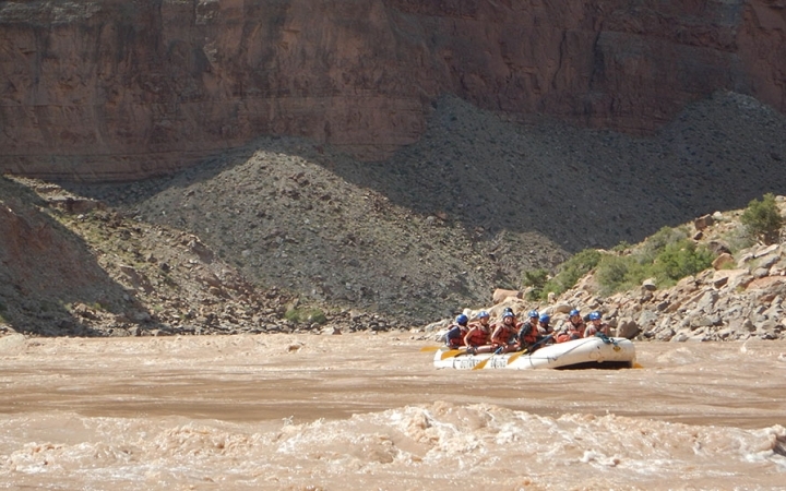 outward bound gap year students paddle a raft on a muddy river surrounded by high canyon walls